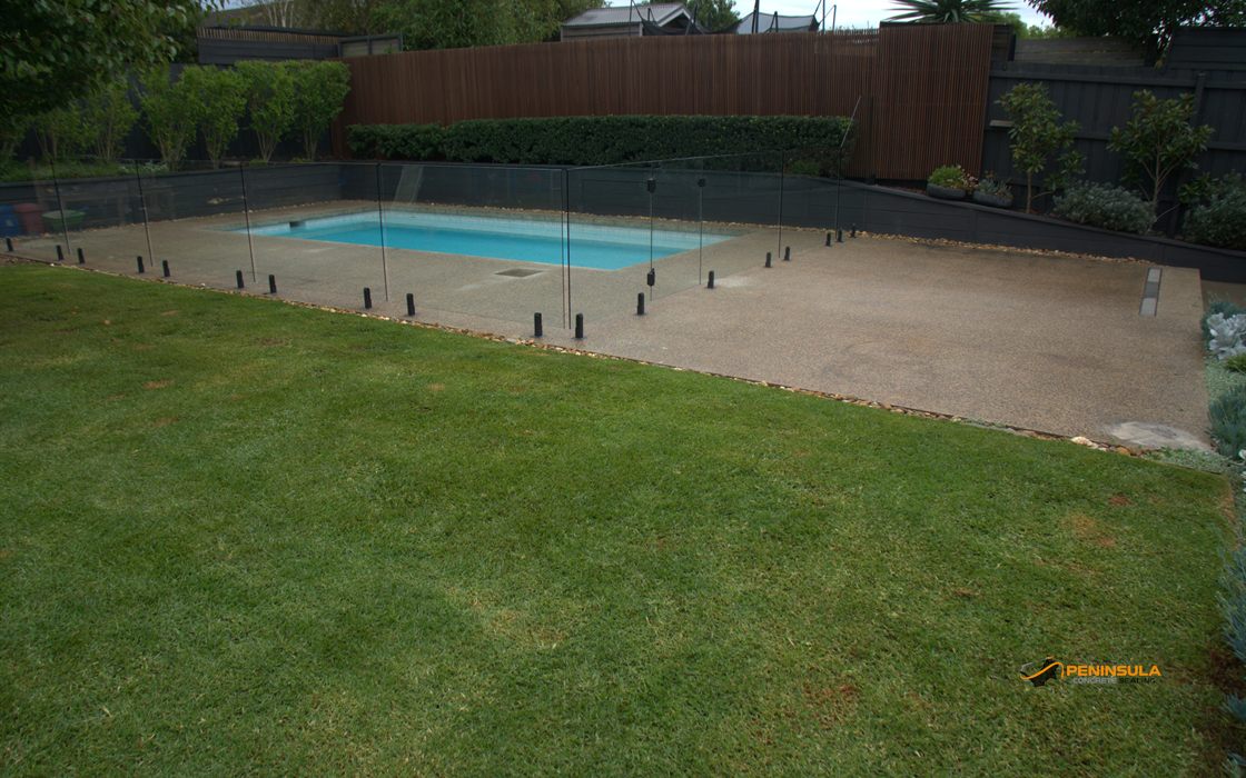 Sealed exposed aggregate pool deck with glass fencing and lawn